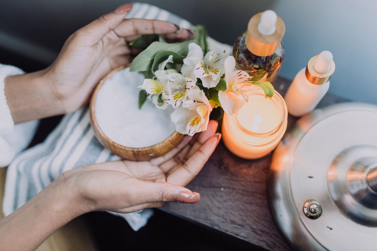 A calming spa scene featuring hands holding flowers beside candles and skincare products.
